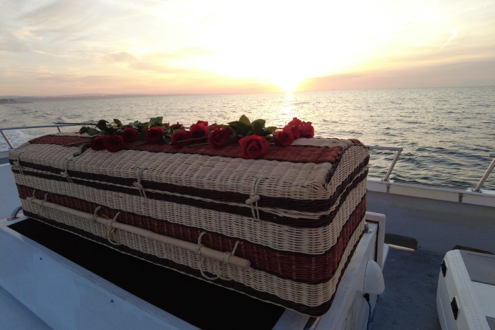 Wicker coffin with red roses on a boat at sunset by the sea.