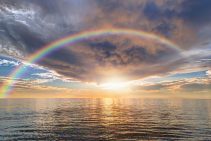 Rainbow over ocean at sunset with dramatic clouds.